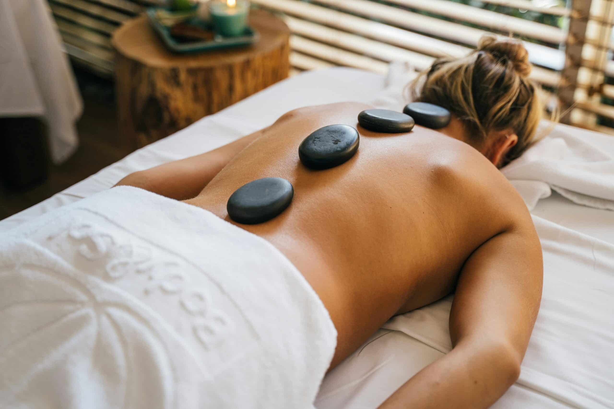 Une femme allongée en position ventrale sur une table de massage avec une serviette de bain autour de la taille et des galets posés sur son dos