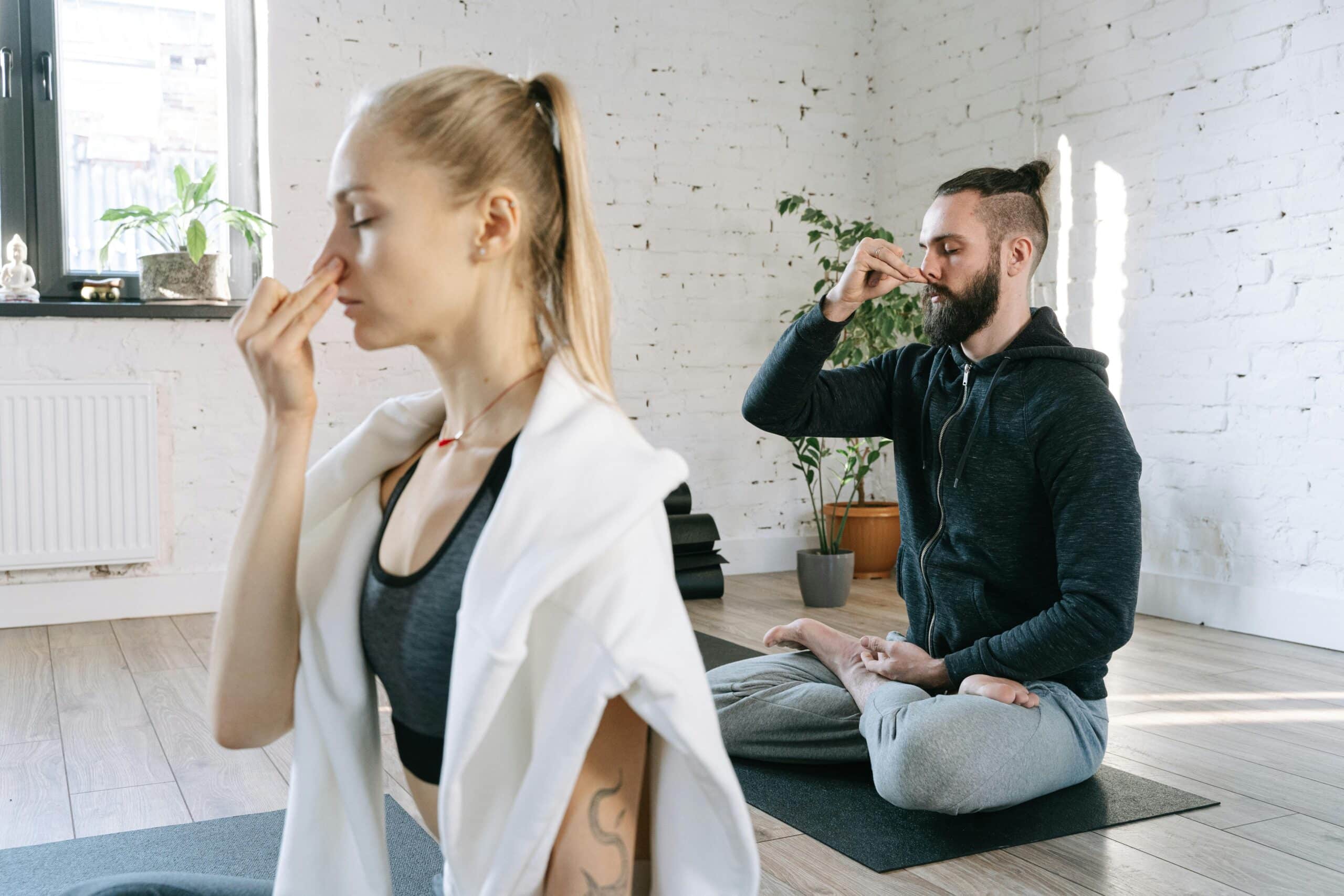 Un homme et une femme assis en tailleur sur un tapis de yoga faisant un exercice de pranayama